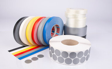 mehrere Gewebeklebebänder und Filamentklebebänder in verschiedenen Farben und Größen liegen auf einer Fläche.