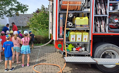 Kindergarten stehen am Hands-On Aktionstag von PRODINGER hilft neben einem Feuerwehrauto und schauen bei einer Löschübung zu.