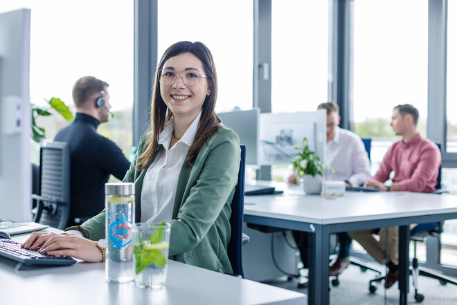 Junge Mitarbeiterin in modernen Großraumbüro an modernen PC-Arbeitsplatz.