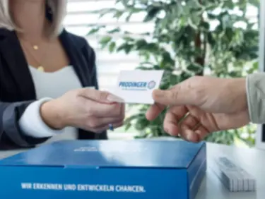 Eine Kundenbetreuerin von PRODINGER überreicht einem Kunden ihre Visitenkarte.