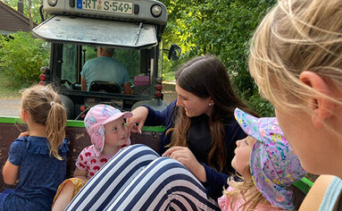 Während einer Ferienbetreuung machen kleine Kinder eine Ausfahrt auf dem Anhänger eines Traktors.