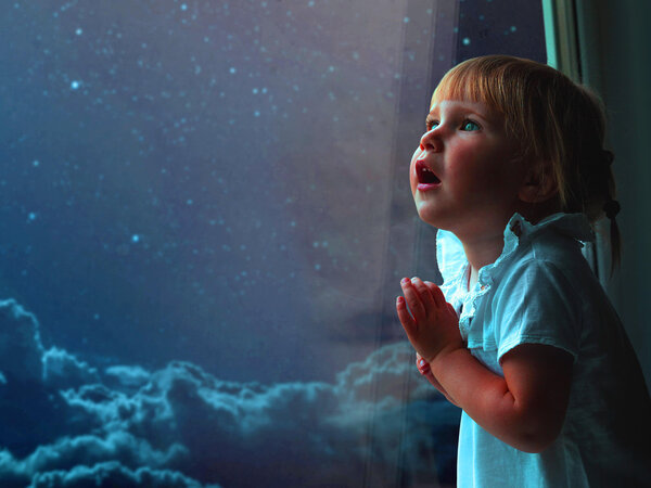 Kleines Mädchen steht am Fenster und blickt staunend in den Sternenhimmel.