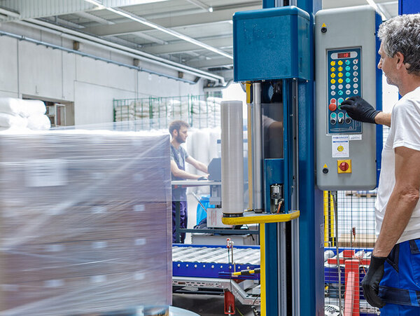 PRODINGER Mitarbeiter bedient Stretchmaschine in der Logistik, im Hintergrund steht weitere Verpackungstechnik