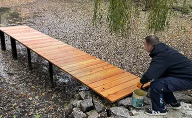 Ein Mitarbeiter von PRODINGER befestigt das letzte Holzmodul an dem Steg des Teiches.