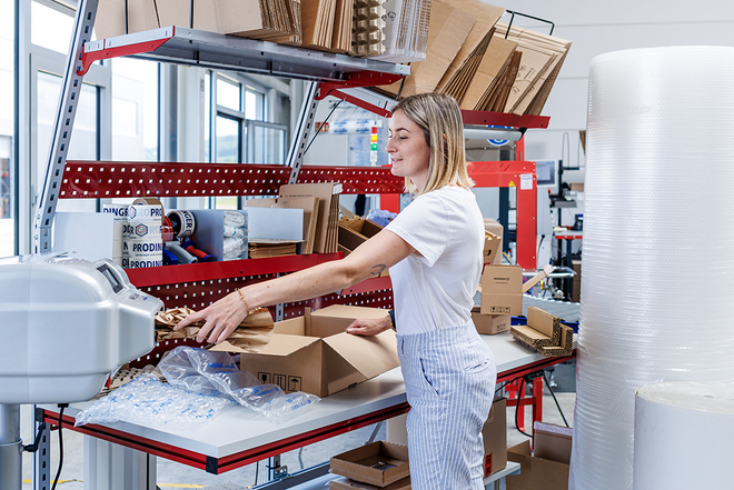 PaperBubble erzeugt Papierpolster, die in die Kartonage an einem Packtisch mit diversen Schutz- und Polstermaterialien, wie z. B. Luftpolsterfolie, zum Schutz des Produkt beigelegt werden.