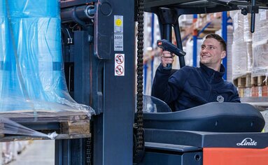 Logistik Ein Logistik-Mitarbeiter der PRODINGER Verpackung sitzt auf einem modernen Stapler und scannt eine Palette aus dem Hochregallager.